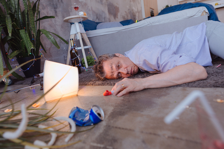 Drunk man. Irritated mature man lying on floor and gazing straightの写真素材