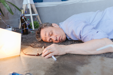 Sign of alcoholism. Inebriate mature man lying on floor and closing eyesの写真素材