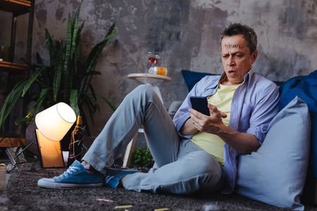 Yesterday history. Amazed mature man using phone and sitting on floor