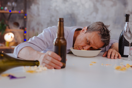 Evidence of alcoholism. Besotted mature man lying in bowl and touching bottleの写真素材