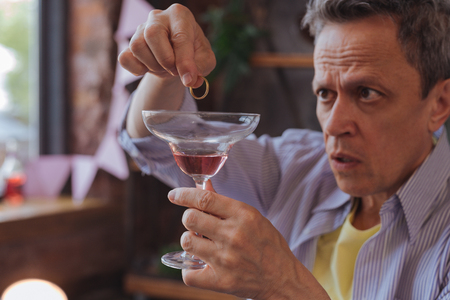 Ring in cocktail. Earnest mature man holding glass and placing ring in itの写真素材