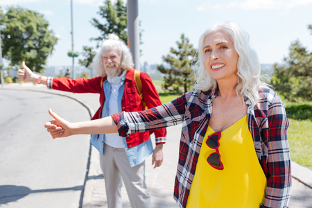 Female hitchhiker. Delighted aged woman smiling while looking for a car for a rideの写真素材