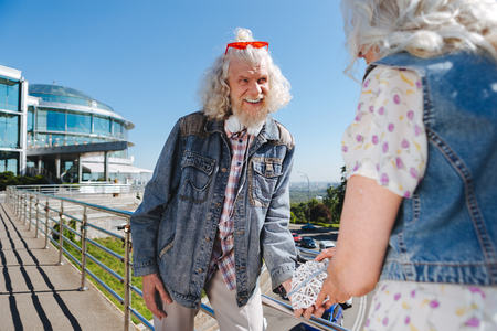Elderly couple. Cheerful aged man looking at his wife while standing with her on the bridgeの写真素材