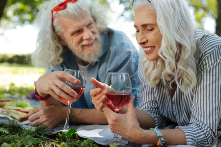 My favourite drink. Cheerful positive woman smiling while looking at the glass with wineの写真素材