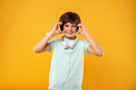 I love technology. Joyful handsome boy holding two phones and wearing headphonesの写真素材