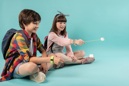 Inspiration. Content lovely schoolchildren holding sticks and sitting next to each otherの写真素材