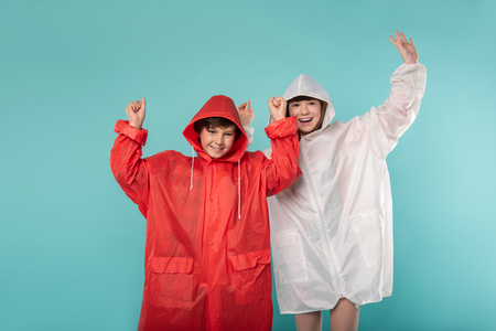 So stylish. Delighted sweet kids standing next to each other and wearing raincoatsの写真素材