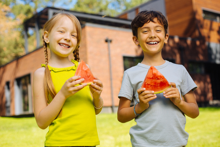 Happiness inside us. Cheerful charming kids smiling and eating a ripe watermelonの写真素材