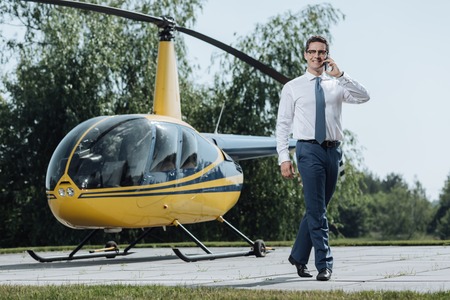 On his way. Upbeat young CEO using his phone and calling taxi from a helipad while walking away from the helicopterの写真素材