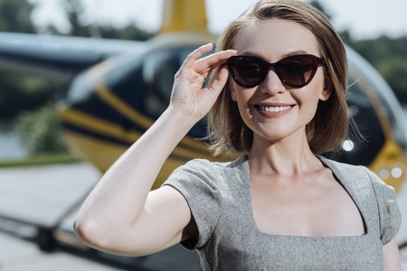 Sunny day. The close up a pretty young businesswoman adjusting her sunglasses while posing at a...
