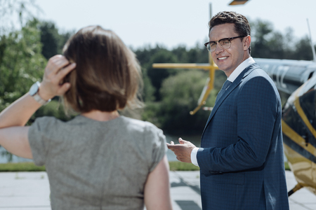 Pleasant interaction. Upbeat young businessman in a suit talking to his female business partner while showing her his private helipadの写真素材