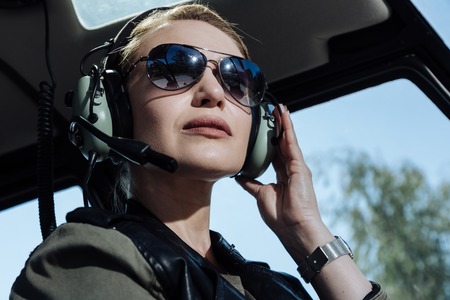 Gorgeous professional. The close up of a pretty young female helicopter pilot sitting listening to air traffic controller in her headphones and being ready to start a flightの写真素材