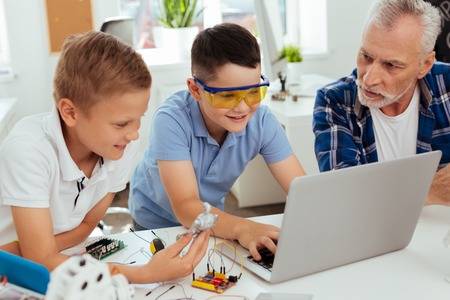 Modern generation. Positive nice boy sitting in front of the laptop while typing on itの写真素材