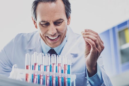 Elderly chemist. Elderly famous skillful chemist wearing blue tie working very hard while looking at test tubesの写真素材