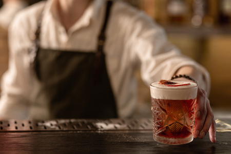 Enjoy it. Young professional man working as a barman and serving a nice newly made cocktail with a burnt sugar on top of itの写真素材