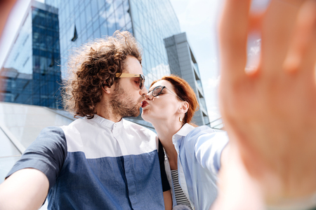 Cute kiss. Cute young woman wearing striped dress feeling really wonderful kissing her curly manの写真素材