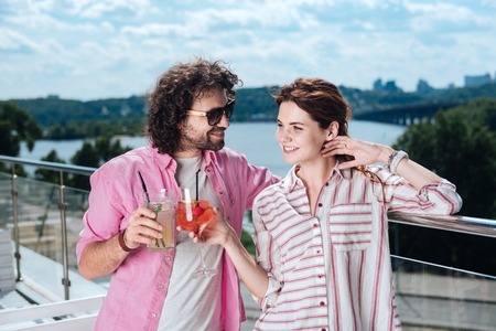 Refreshing cocktails. Curly man wearing sunglasses drinking refreshing summer cocktail with his womanの写真素材