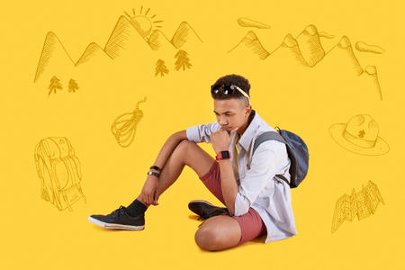 Thinking. Calm concentrated traveler sitting on the ground and thoughtfully touching his chin while considering his future journeyの写真素材