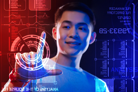 Transparent screen. Cheerful confident programmer smiling and touching the round diagram on the screen while working at the programの写真素材