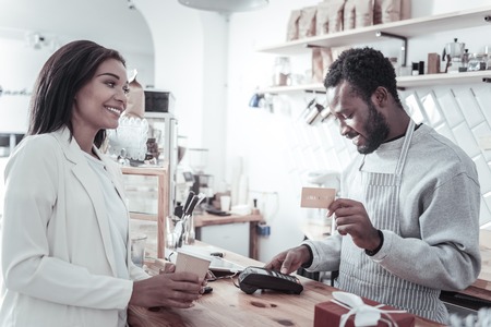 Modern banking. Nice pleasant smart man holding a credit card and making a money transaction while taking a paymentの写真素材