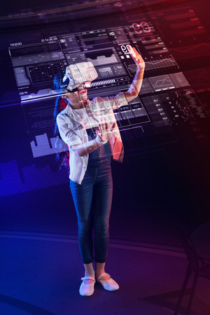 Detailed projection. Smart progressive girl wearing virtual reality device and feeling interested while wearing modern virtual reality glassesの写真素材