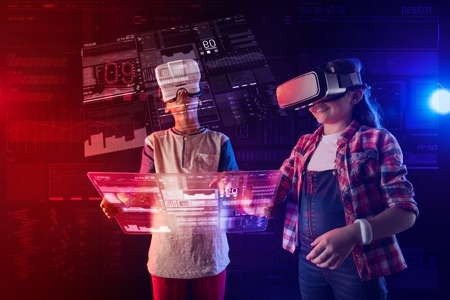 Unusual device. Clever modern kids wearing virtual reality glasses and feeling curious while holding...