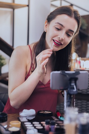 Near table. Dark-haired appealing charming student sitting near makeup table in her living roomの写真素材