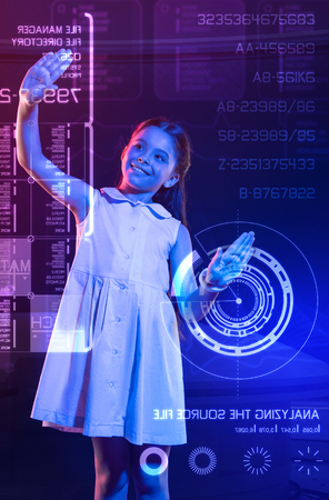 Confident girl. Cheerful girl wearing a lovely dress and smiling while putting to hands on the screen of a transparent deviceの写真素材