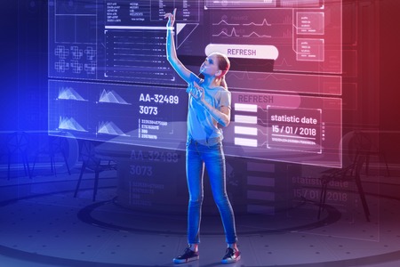 High screen. Calm attentive teenage girl putting her hand up and looking at the information on the transparent screen while touching the icons on itの写真素材