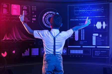 Global research. Concentrated clever pupil putting his hands up and touching the transparent screen while making a big researchの写真素材