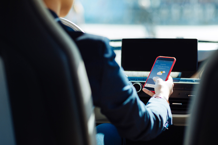 Digital technology. Close up of a modern smartphone being in hands of a nice female driver while checking the weatherの写真素材