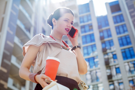 Distance communication. Pleasant young woman making a call while going from the officeの写真素材