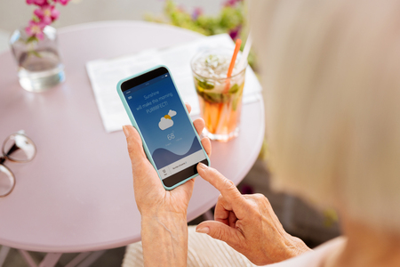 Weather for tomorrow. Close up of mature female hands carrying phone and using app for weather forecastの写真素材