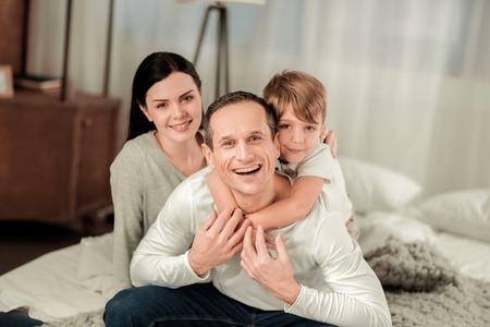 Happiness and joy. Positive nice boy hugging his father while sitting behind himの写真素材