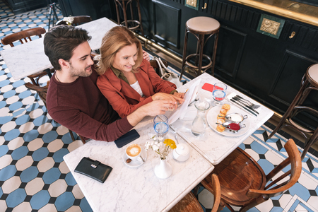 Romantic restaurant. Top view of loving attractive couple choosing meal and pointing at menuの写真素材