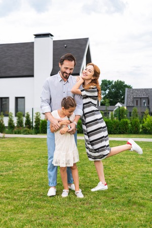 Our home. Delighted positive family standing near their house while enjoying being togetherの写真素材