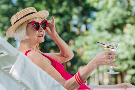 Blonde-haired grandmother. Blonde-haired grandmother wearing stylish hat relaxing outside near the poolの写真素材
