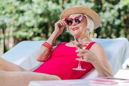 Rest near pool. Blonde-haired mature woman feeling extremely happy while having rest near poolの写真素材