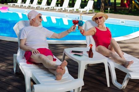 Birthday celebration. Mature woman celebrating her birthday with loving husband while sunbathing near poolの写真素材