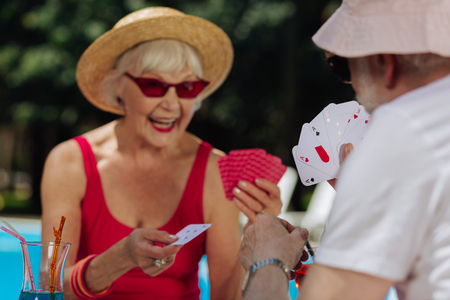 White shirt. Retired bearded man wearing white shirt playing cards with wife while sitting near...