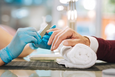 Manicure in steps. Close up of female hands dressing in gloves and applying fileの写真素材