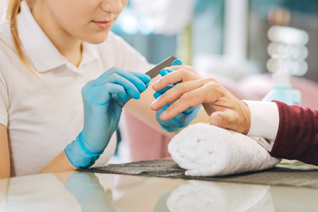 Perfect manicure. Close up of female hands putting on gloves and using fileの写真素材