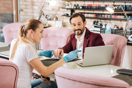 During manicure. Woman pointing at screen and joyful mature man using laptopの写真素材
