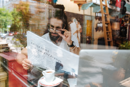 Morning news. Nice smart man fixing his glasses while reading a newspaperの写真素材