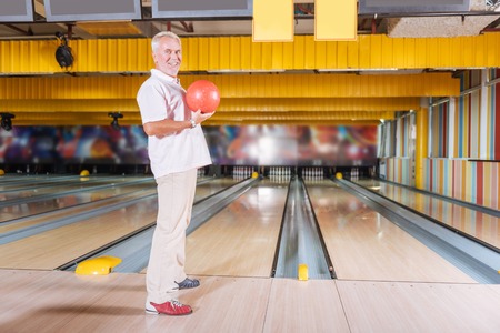 My turn. Pleasant joyful man holding a bowling ball while preparing to hit skittlesの写真素材