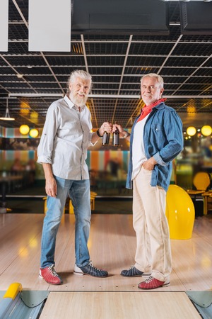 Favourite drinks. Delighted nice men standing together while holding bottles of beerの写真素材