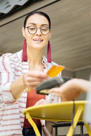 Easy payment. Positive visitor of a local cafe smiling while using a credit card and paying with a...