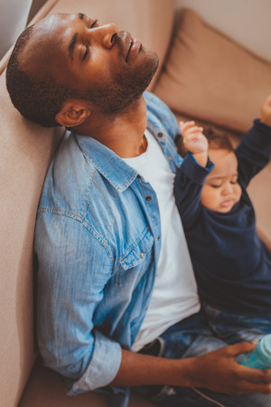 Daydreaming. Young afro-american daddy sleeping while babysitting his little sonの写真素材