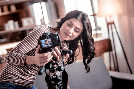 Great gadget. Smiling dark-haired woman fixing her camera while making a video for her blogの写真素材