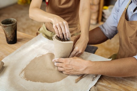 Making vase. Skillful creative woman with dark nail art helping potter with making vase in workshopの写真素材